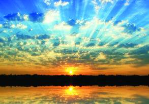 Sunset over a tranquil lake, with the sun's last words creating a golden reflection on the water and sunbeams radiating through scattered clouds in a vibrant blue sky.