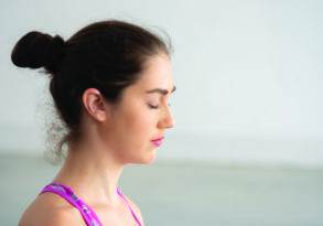 A woman with a bun hairstyle and a tape measure draped over her shoulders, eyes closed in mindfulness, profile view.