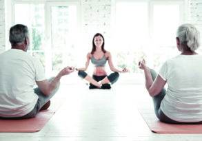 A yoga instructor leads a senior couple in a meditation session in a bright, airy room, emphasizing companionship and aging together.