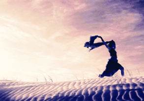 Silhouette of a dancer performing on sand dunes at twilight, her hands gracefully positioned above her head, symbolizing the strength and grace in breast cancer awareness.