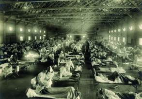 Historic photo of a large indoor hospital ward filled with rows of beds and patients during the 1918 Flu Epidemic, with nurses and a doctor present, early 20th century.