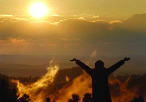 Silhouette of a person with raised arms facing a sunset over a misty forest landscape, embodying a moment of spirituality.