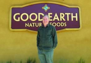 A man smiling in front of a "Good Earth Organic Foods" store sign.