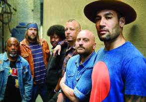 Group of six diverse men posing casually against a textured wall at the Common Ground Festival, displaying a range of expressions and styles.