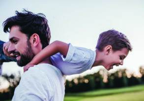 A young boy enjoys a piggyback ride on a man's back, both smiling and experiencing male development outdoors.