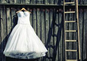 A white wedding dress hanging on a wooden hanger against a weathered wooden wall with a wooden ladder to the side, symbolizing the journey of moving on from a past relationship.