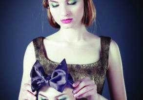 A woman holding a large bow over the head of another woman's portrait, both dressed in vintage attire against a dark background, illustrating symptoms of imposter syndrome.