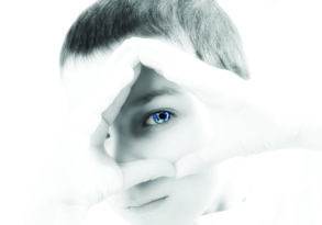 A young boy with fresh eyes upon the world forms a diamond shape with his fingers around his eye, against a high-key, all-white background.