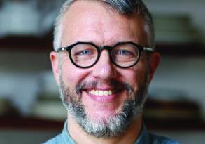 Middle-aged man with a gray beard and glasses smiling at the camera, known for his love of organic food.